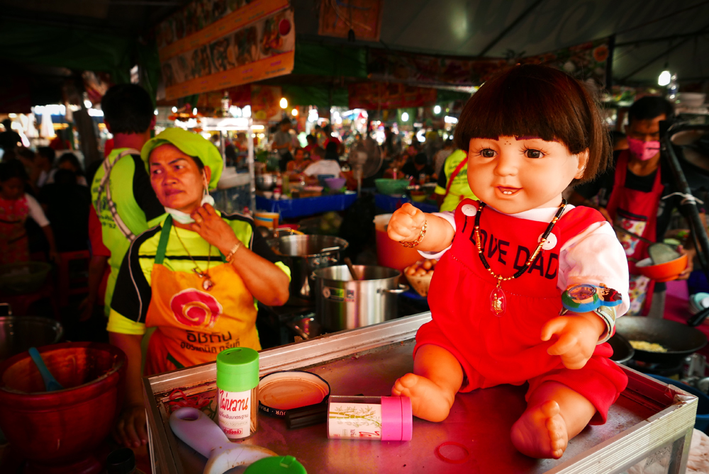 Thaimaassa uskotaan, että Luk Thep -nuket on otettava mukaan jokapäiväiseen elämään, jotta niihin taiottu lapsihenki toisi omistajalleen onnea ja menestystä. Tämä nukke katselee omistajansa työntekoa Chatuchackin viikonloppumarkkinoilla Bangkokissa. Kuva: Saara Alhopuro.