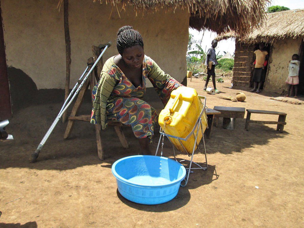 Afrikkalainen nainen kaataa kanisterista vettä vatiin talon edessä