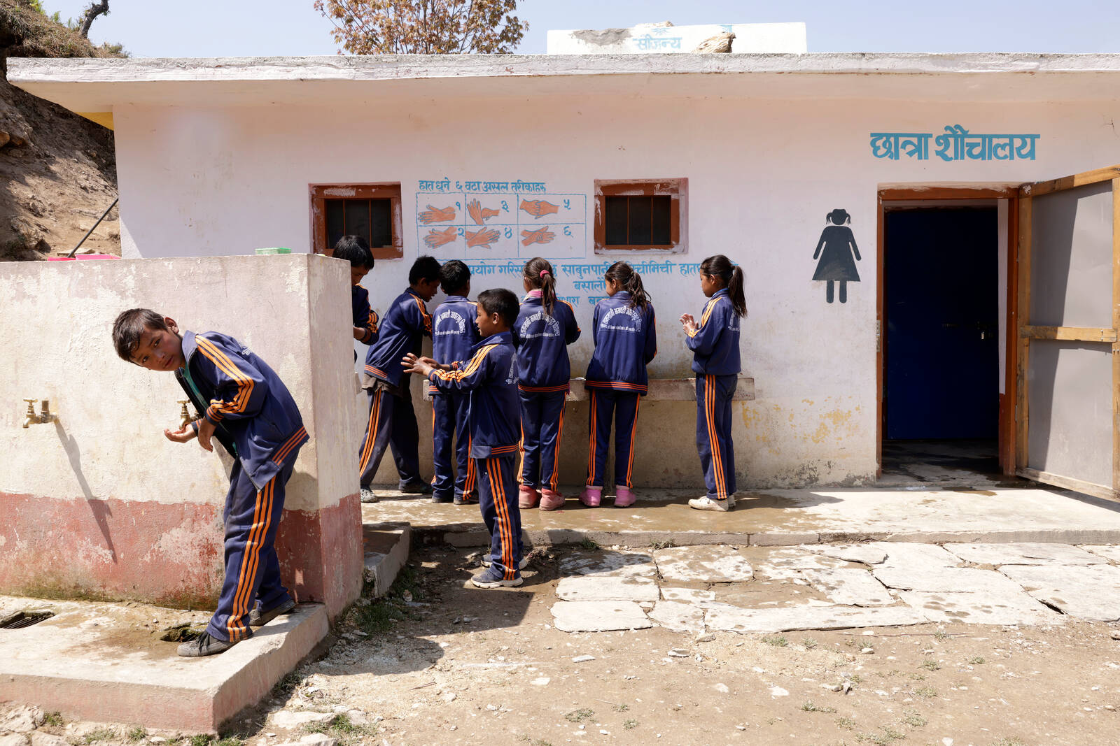 Ryhmä koululaisia pesee käsiään wc-rakennuksen edessä Nepalissa.