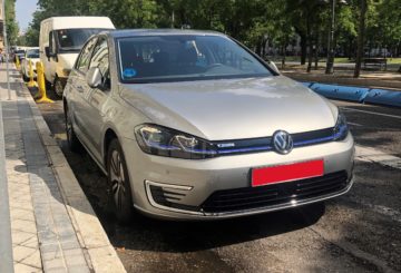 Harmaa Volgswagen-merkkinen sähköauto parkkeerattuna kadulle.