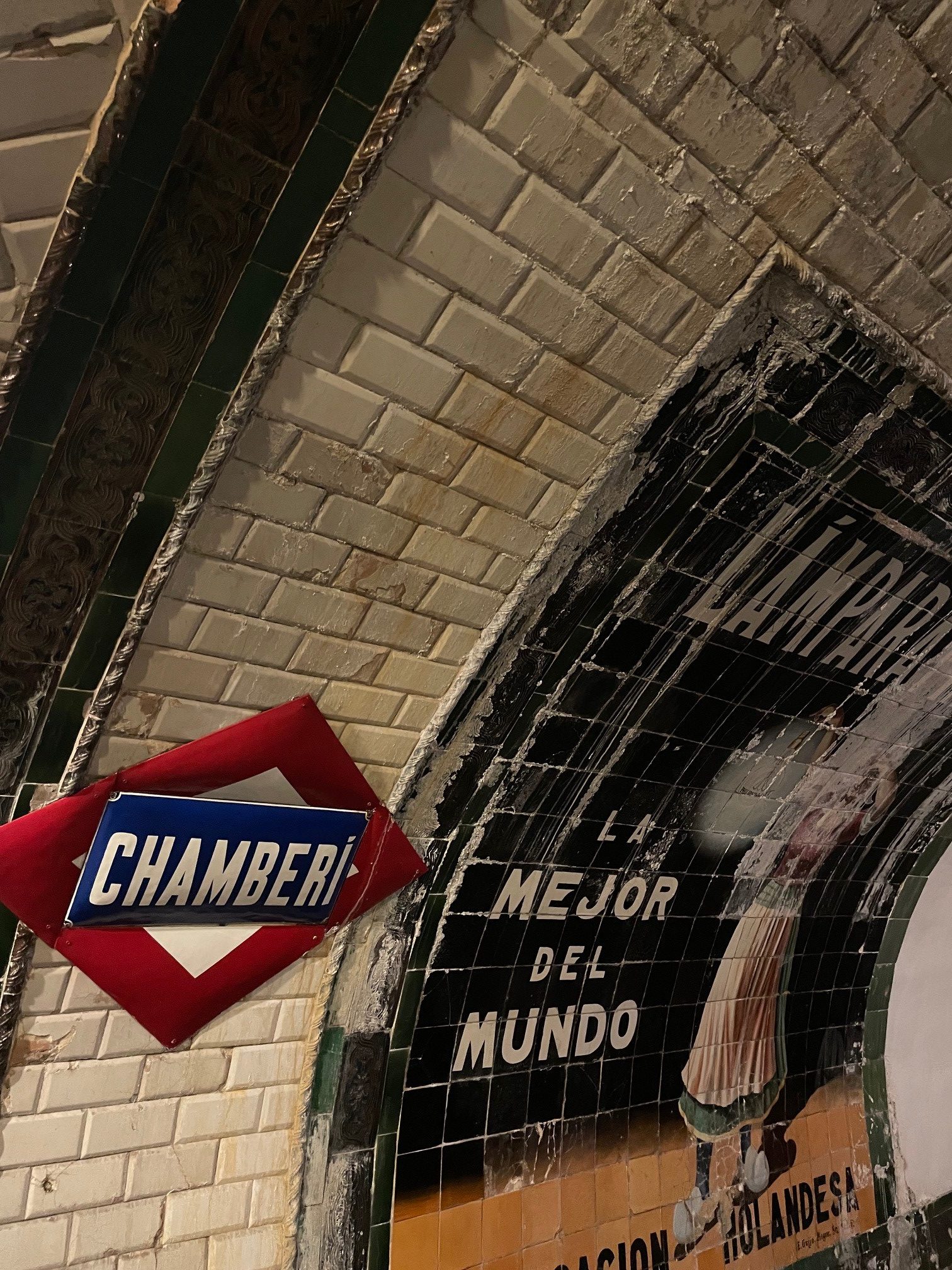 Vanhanaikaisen metroaseman selustaa. Seinässä punasinivalkoinen kyltti, jossa teksti "Chamberi" sekä vanhanaikainen mainoskuva. 