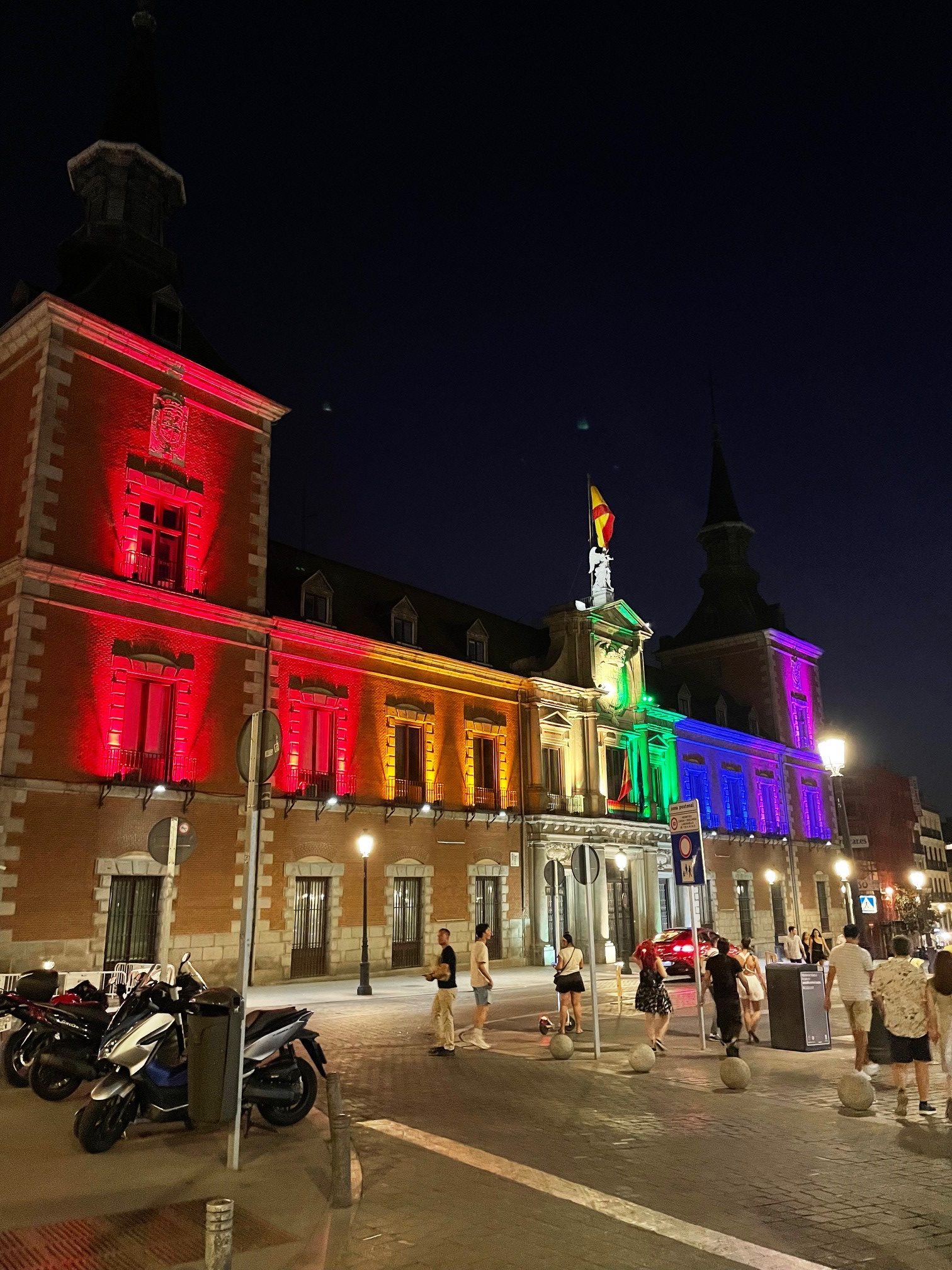 Sateenkaaren värein valaistu oikeusministeriön rakennus kaupunkinäkymässä.